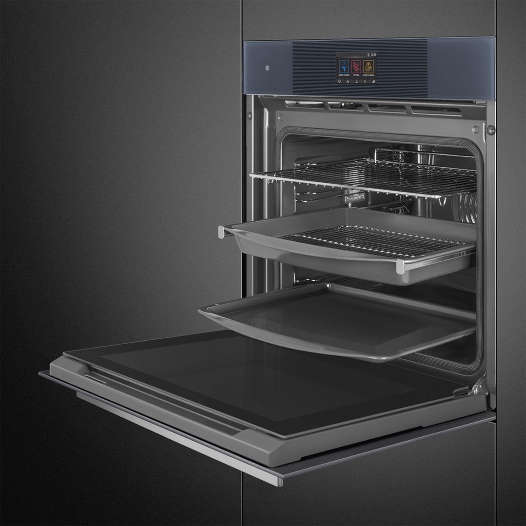 Open built-in oven with racks and trays in a dark kitchen setting
