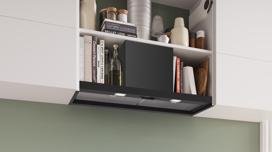 Black Bosch rangehood integrated into white kitchen cabinetry with cookbooks and decor
