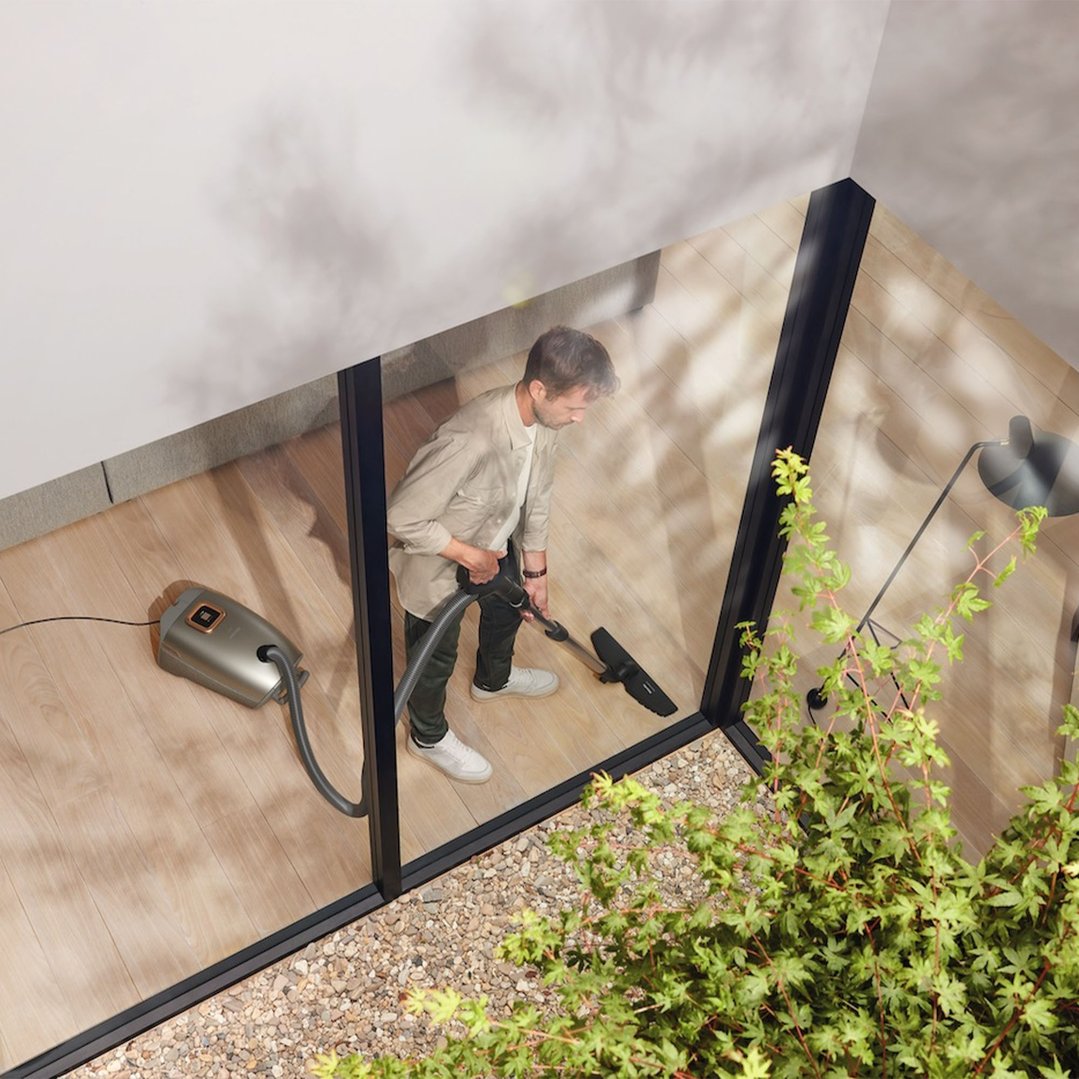 Man vacuuming a wooden floor with a Miele vacuum cleaner