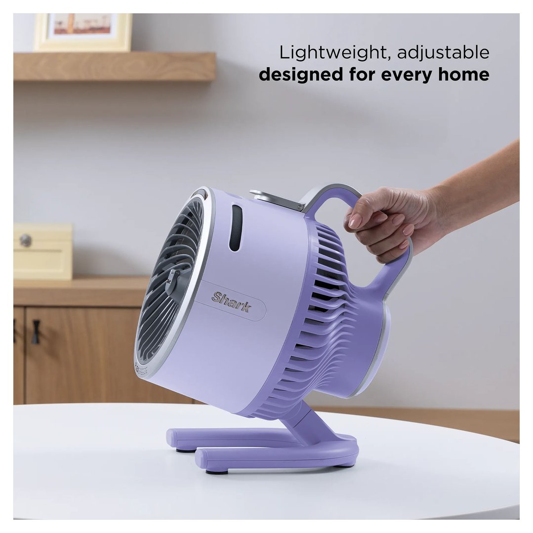 Hand holding a lilac Shark portable fan on a white table