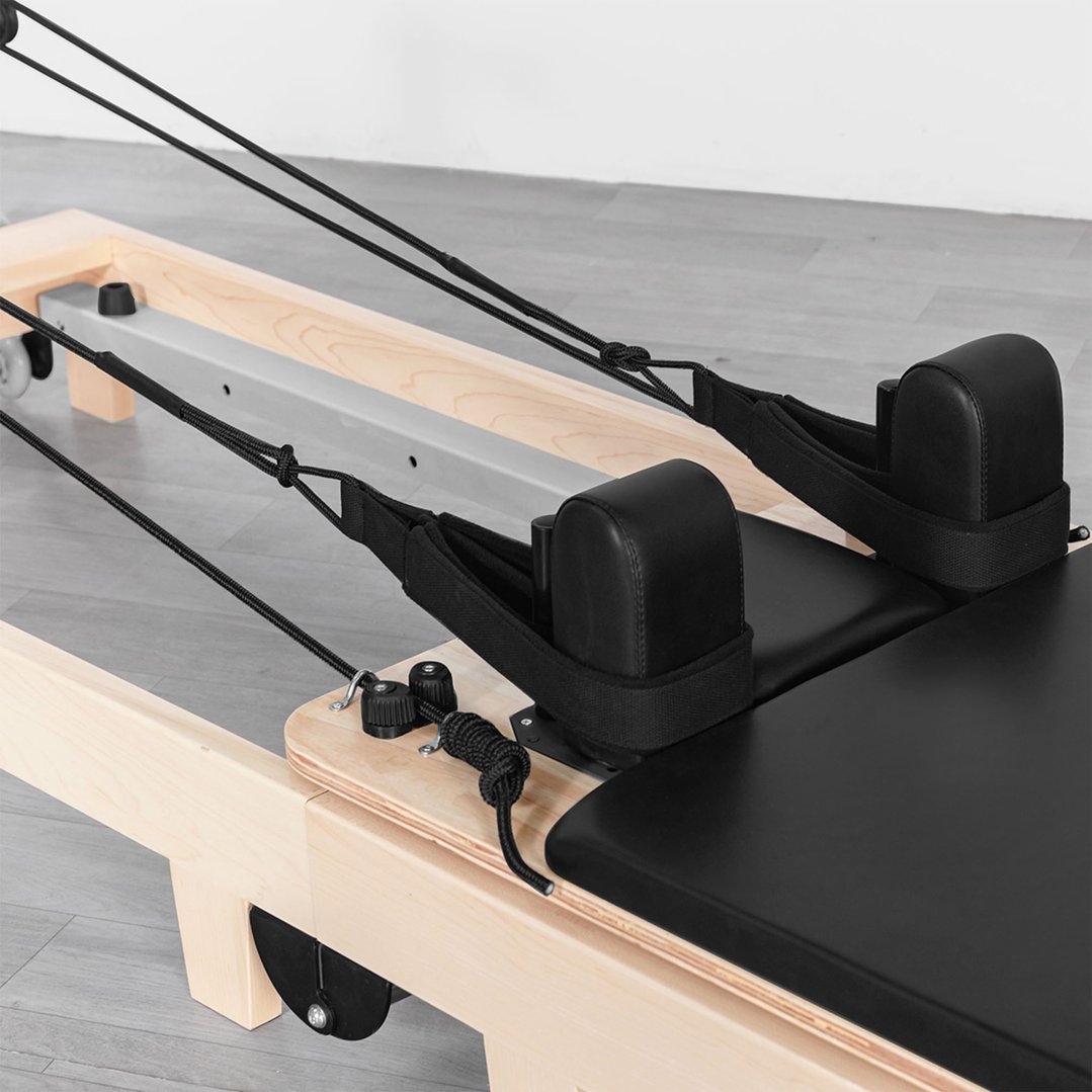 Close-up of the black padded carriage and ropes of a Pilates reformer machine