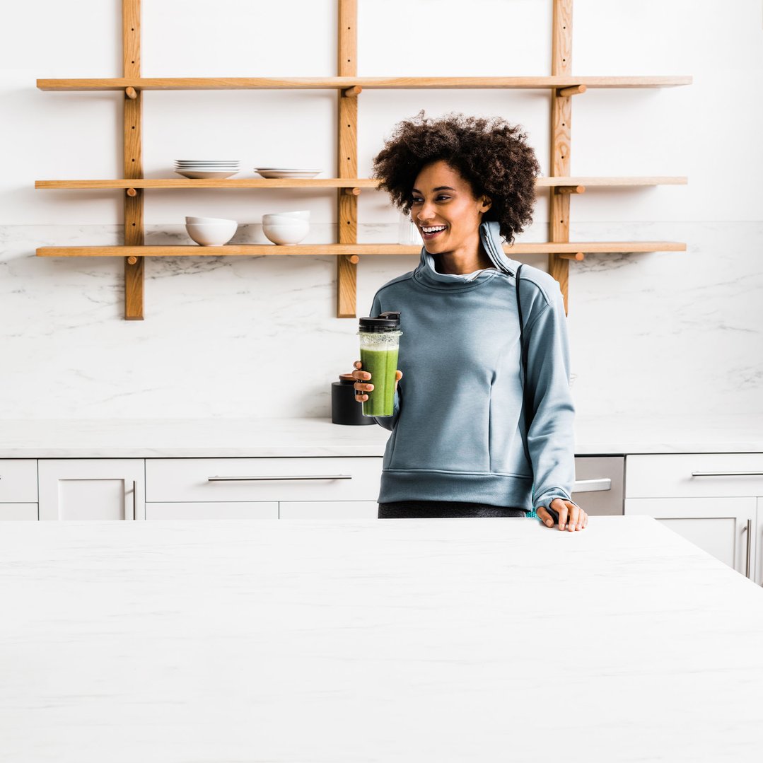 Woman holding a blender with a green smoothie in a modern kitchen