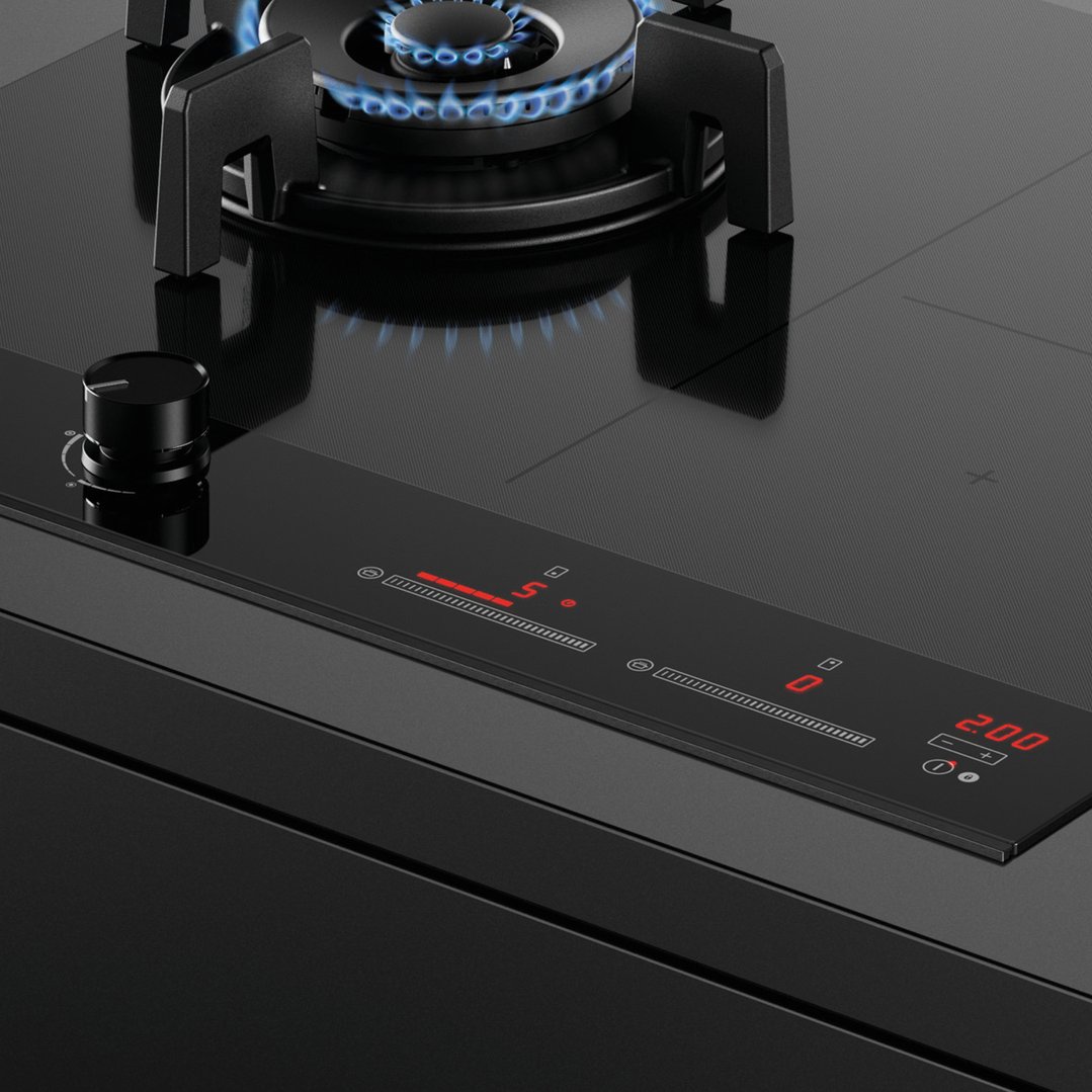 Close-up of a hybrid cooktop with a gas burner lit and digital controls