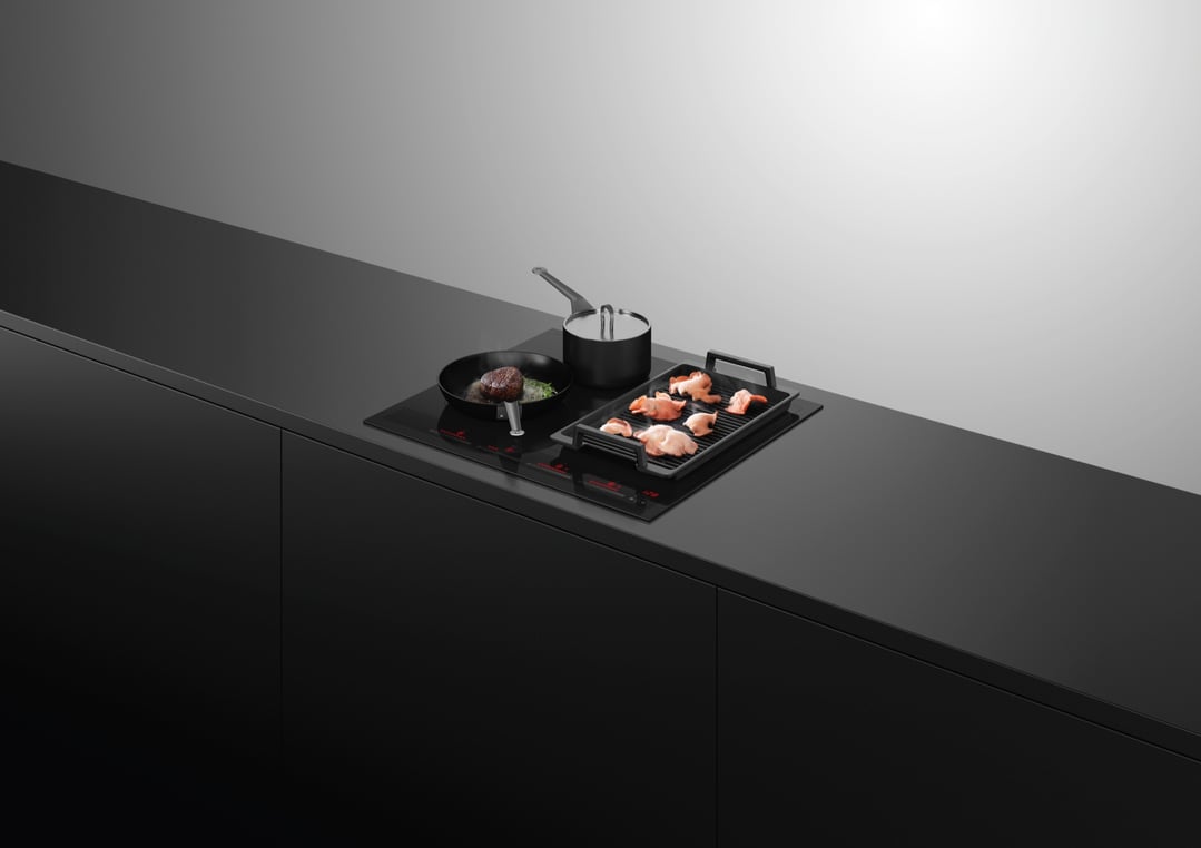 Induction cooktop with a pan and grill cooking food on a black countertop