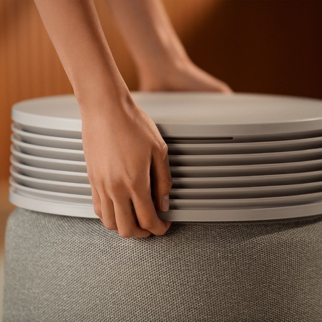 Hands adjusting the top of a light grey air purifier