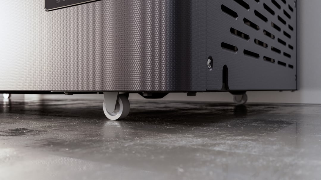 Close up of the bottom of a grey chest freezer with wheels on a concrete floor