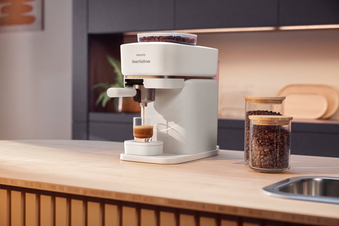 Philips Baristina Espresso Machine dispensing coffee into a glass on a wooden counter