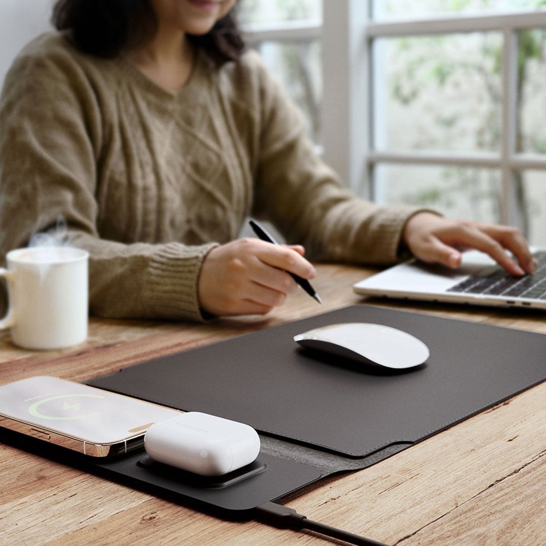 Woman working at desk with laptop sleeve, charging phone and earbuds