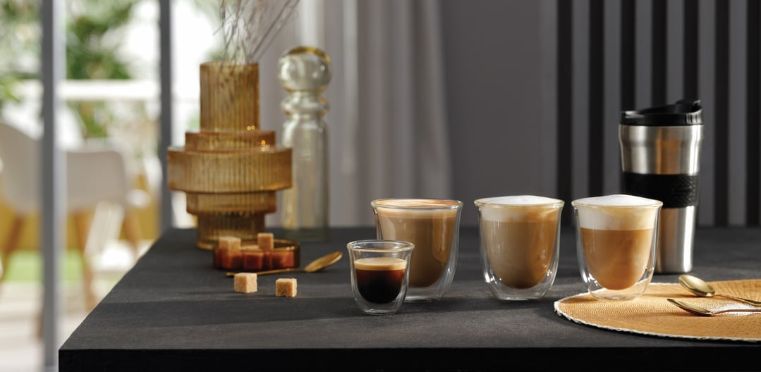 Various coffee drinks in glass cups and a travel mug on a dark countertop