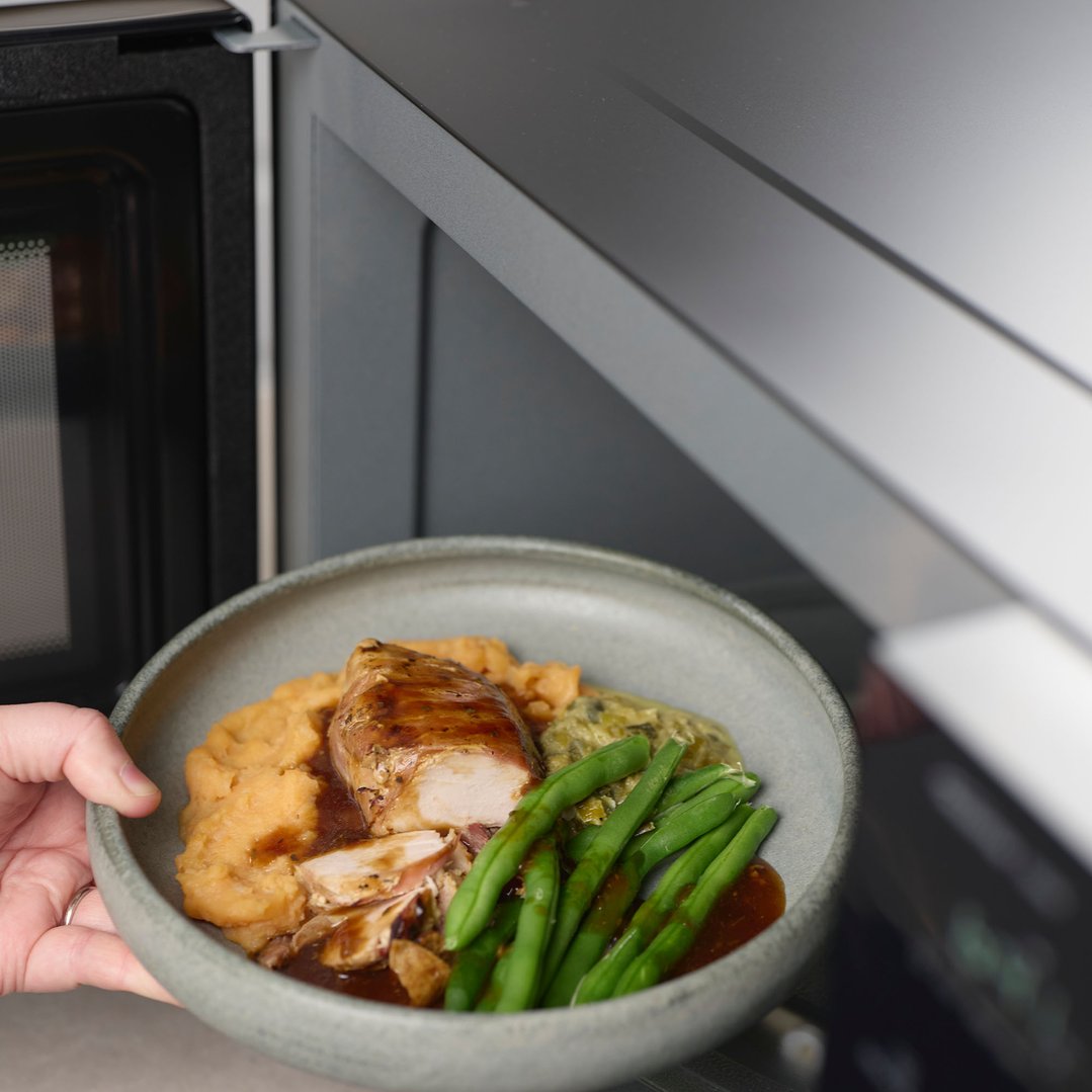 Hand placing a plate of food into a Panasonic microwave