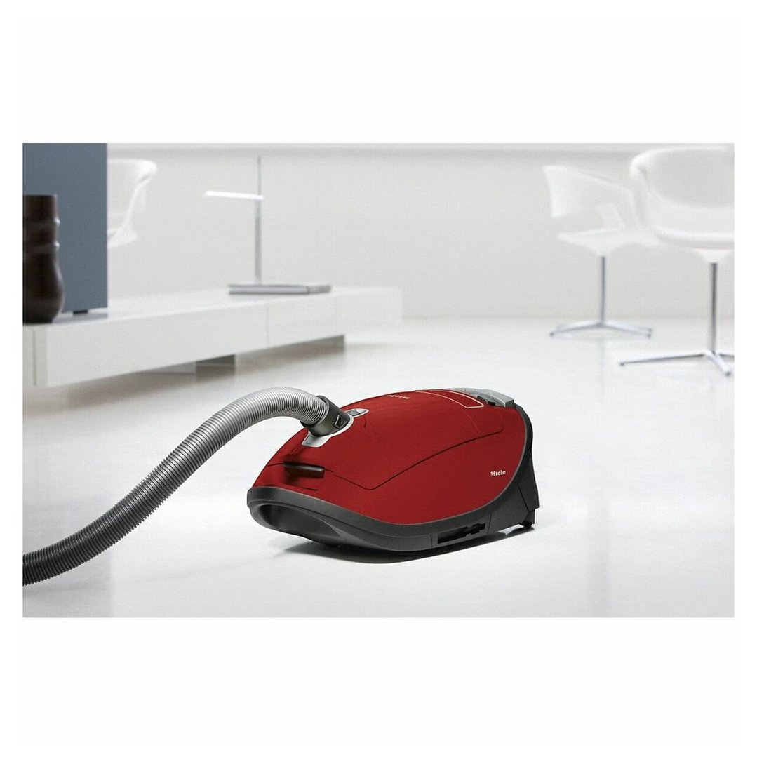 Red Miele vacuum cleaner with hose on a white floor in a modern room