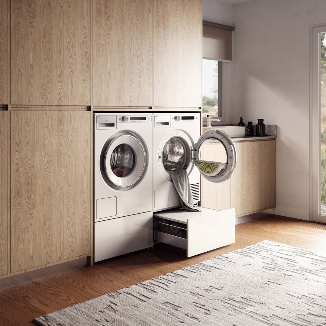 Laundry room with two white washer and dryer units and wooden cabinetry