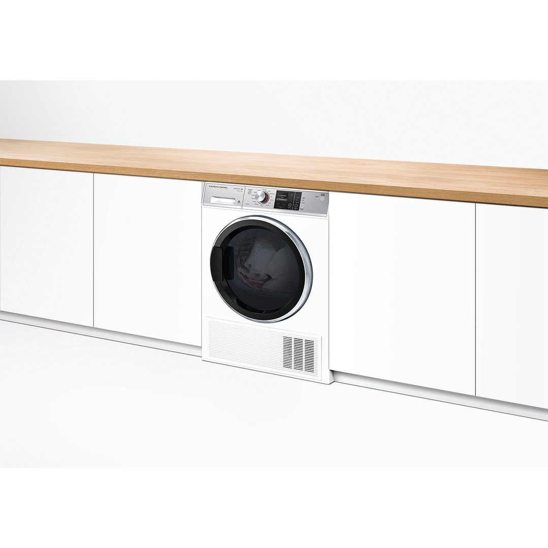 White dryer integrated into white cabinetry with a wooden countertop in a laundry