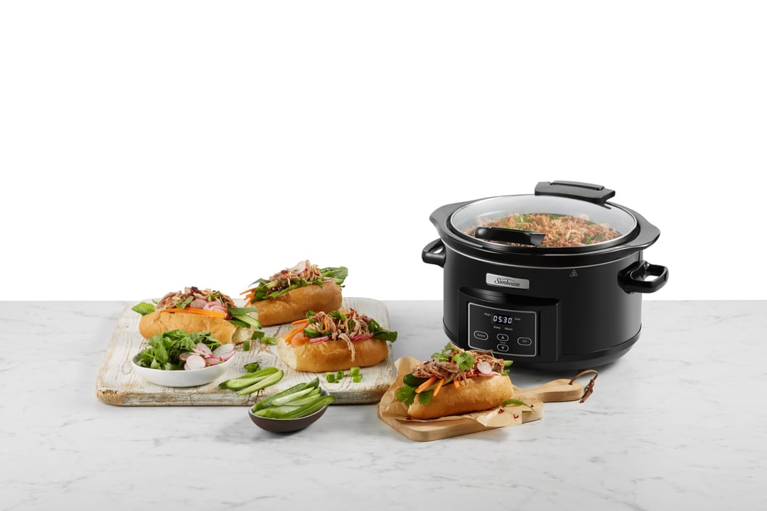 Black Sunbeam slow cooker on a white marble counter with banh mi sandwiches