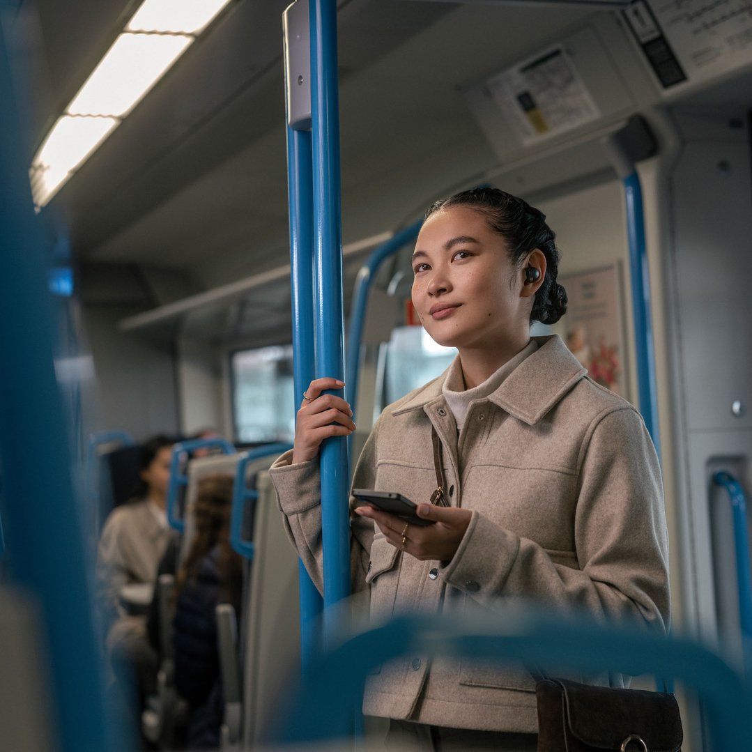 Woman wearing black Truly Wireless Earbuds on a train holding a phone