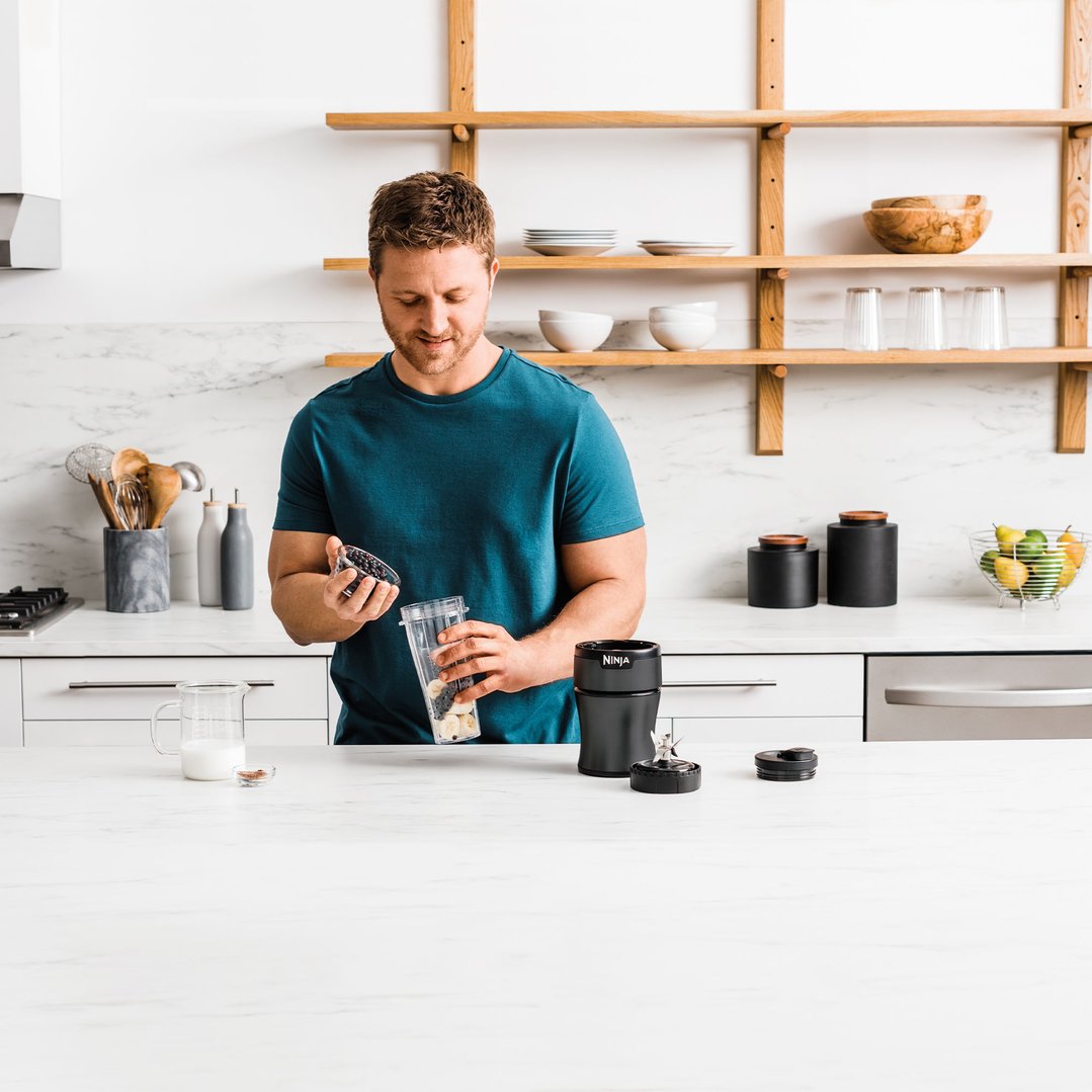 Man adding blueberries to a blender cup in a modern kitchen