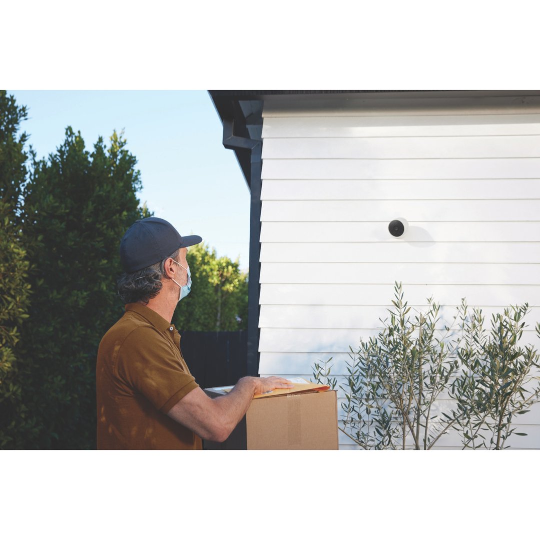 A delivery person wearing a mask delivering a package to a house with a security camera