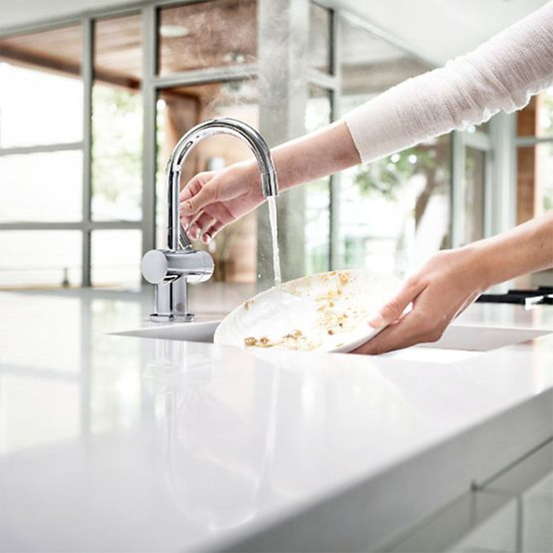Hands rinsing a dirty plate under a chrome hot and cold water tap