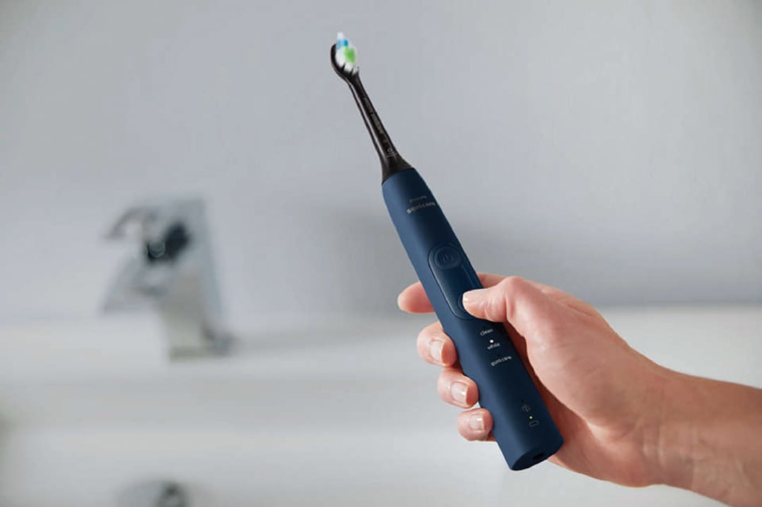 Hand holding a Philips Sonicare electric toothbrush in a bathroom setting