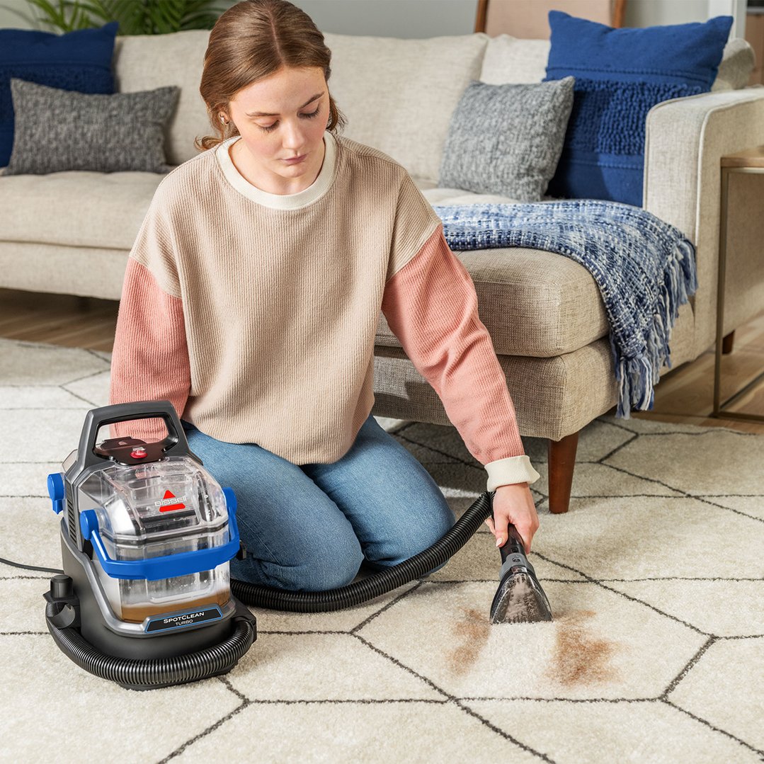 Woman cleaning a stain on a rug with a BISSELL SpotClean Turbo vacuum cleaner