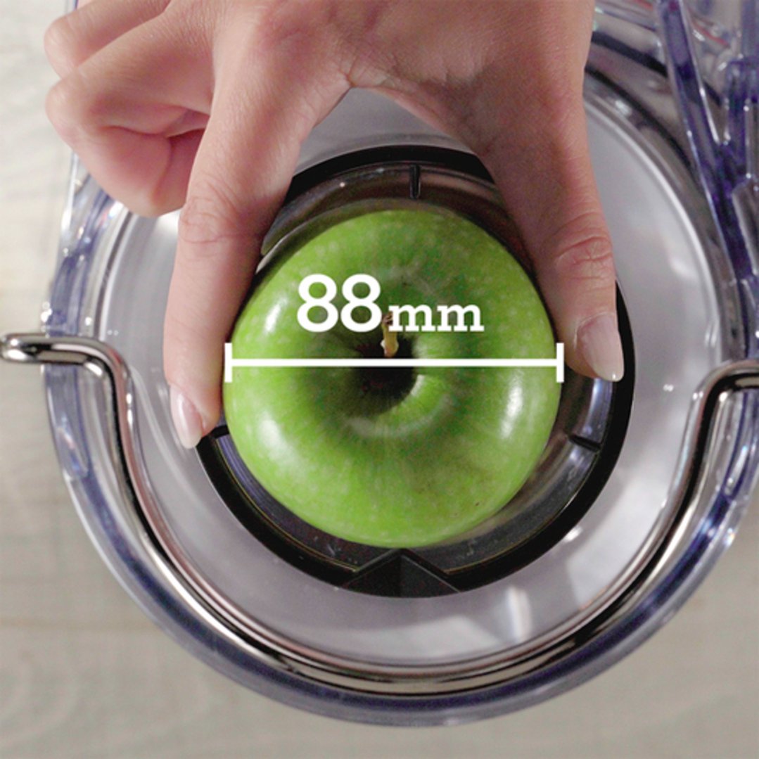 Hand placing an 88mm green apple into the juicer's feed chute