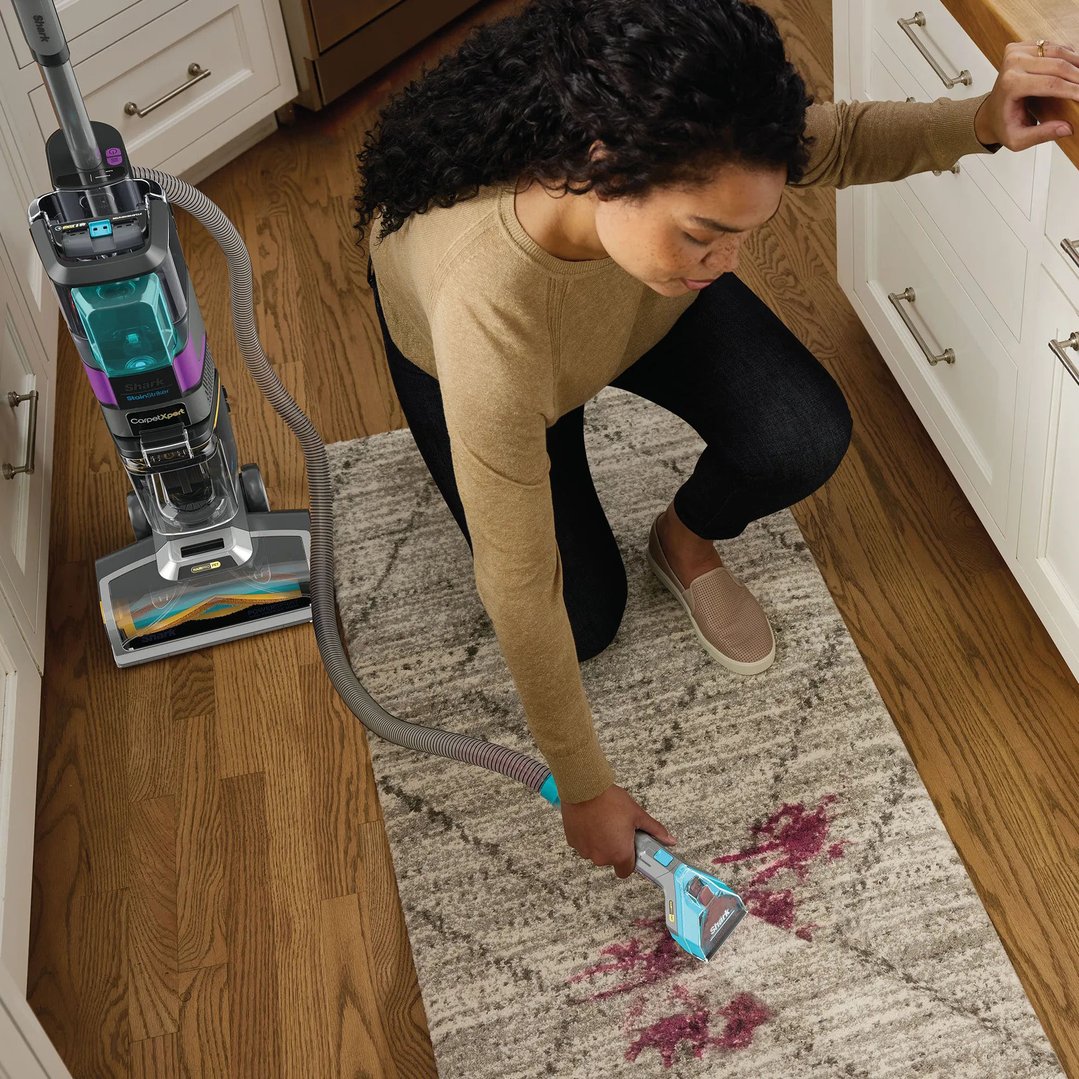 Woman using a Shark vacuum cleaner to clean a red stain on a rug