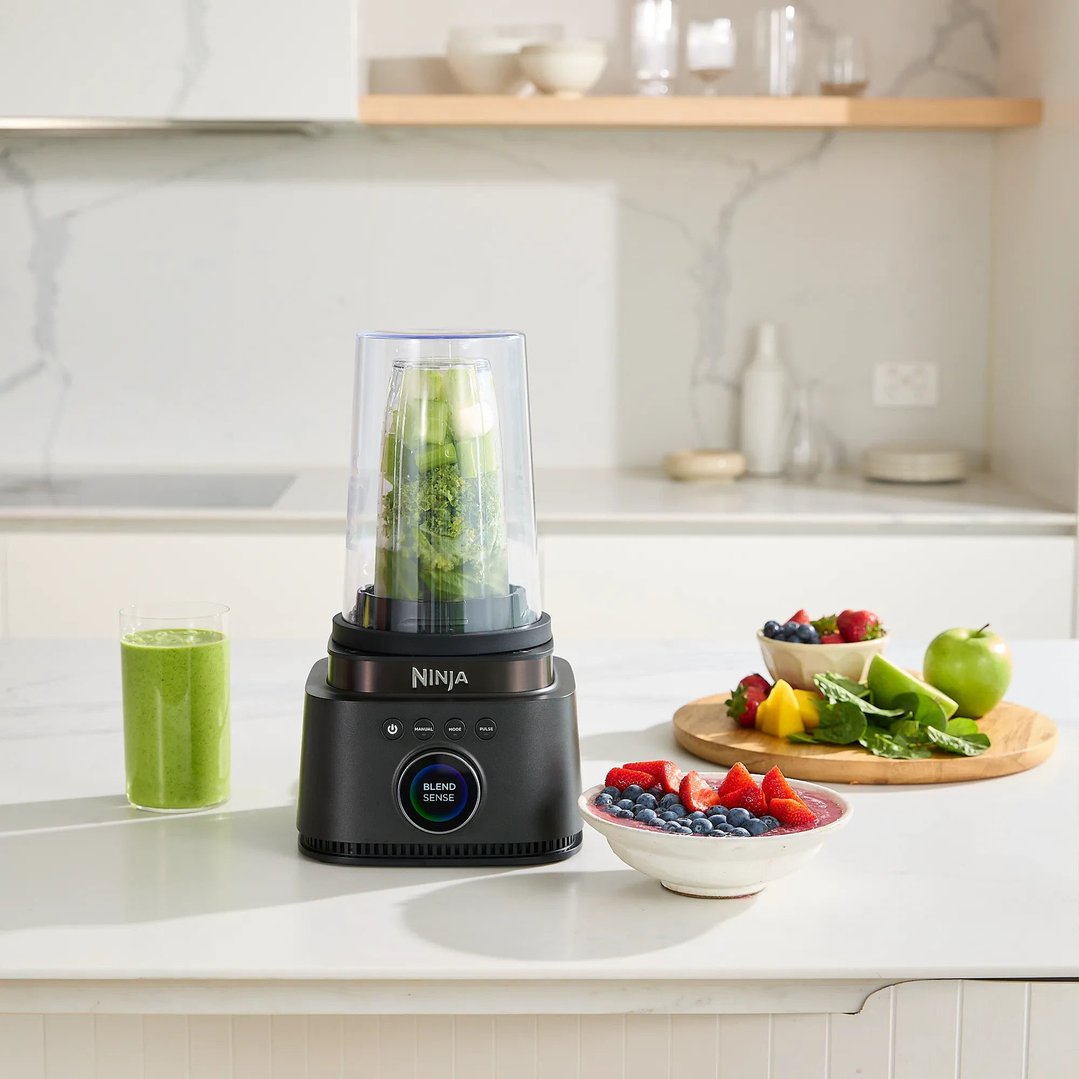 Ninja blender on a kitchen counter with a green smoothie and fresh fruit