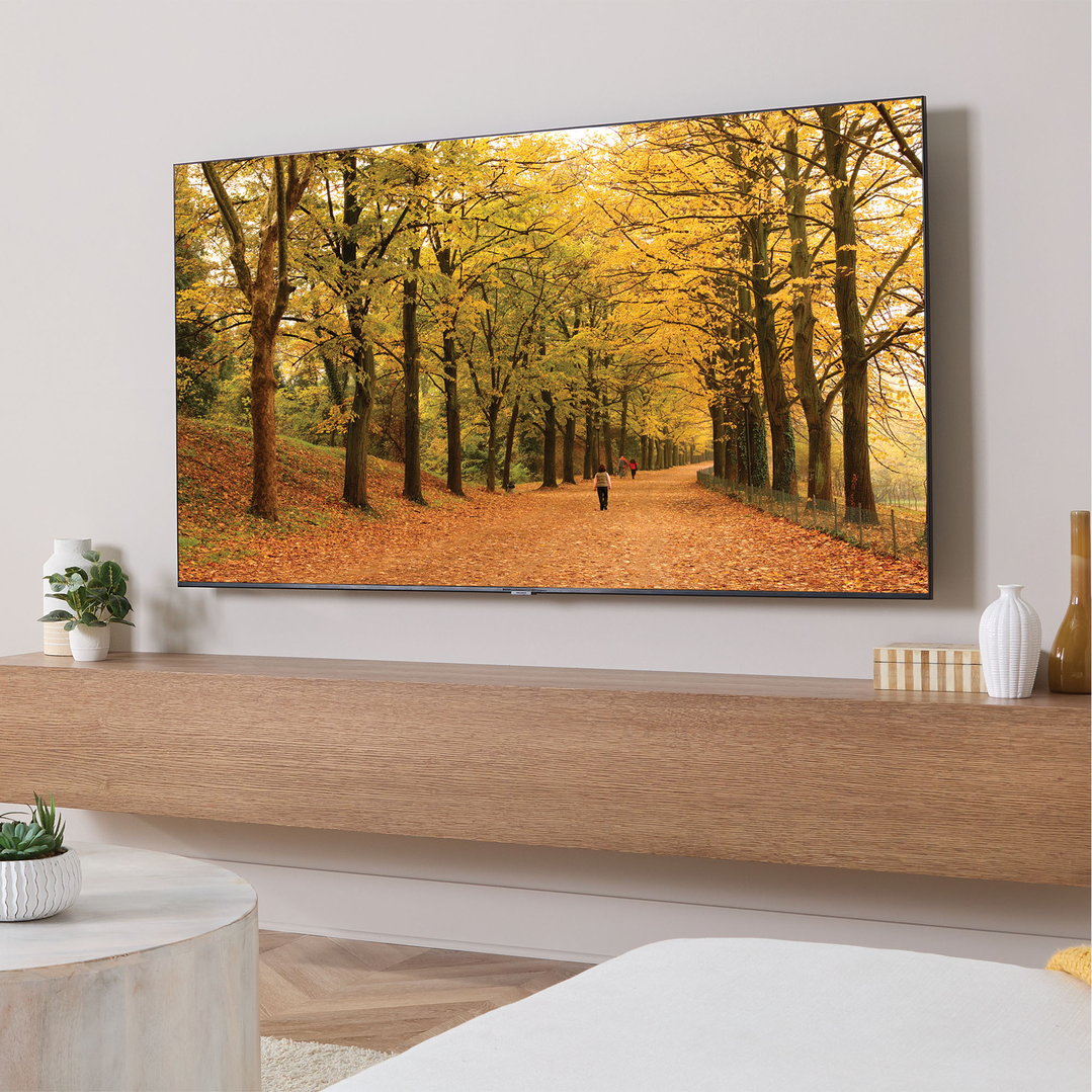 A large TV displaying an autumn forest scene, mounted on a wall