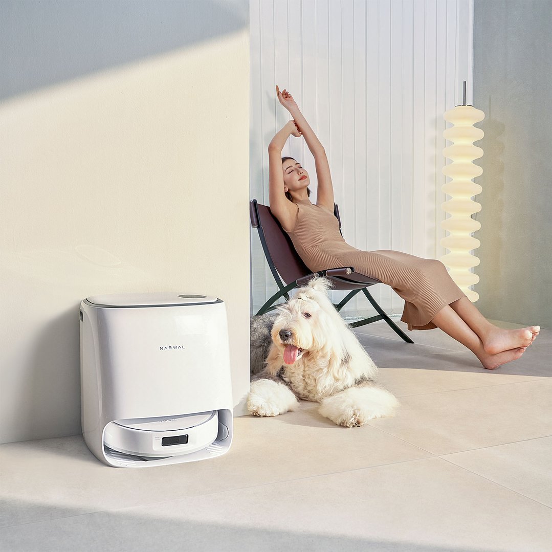Robotic vacuum and mop next to a woman and dog relaxing in a living room