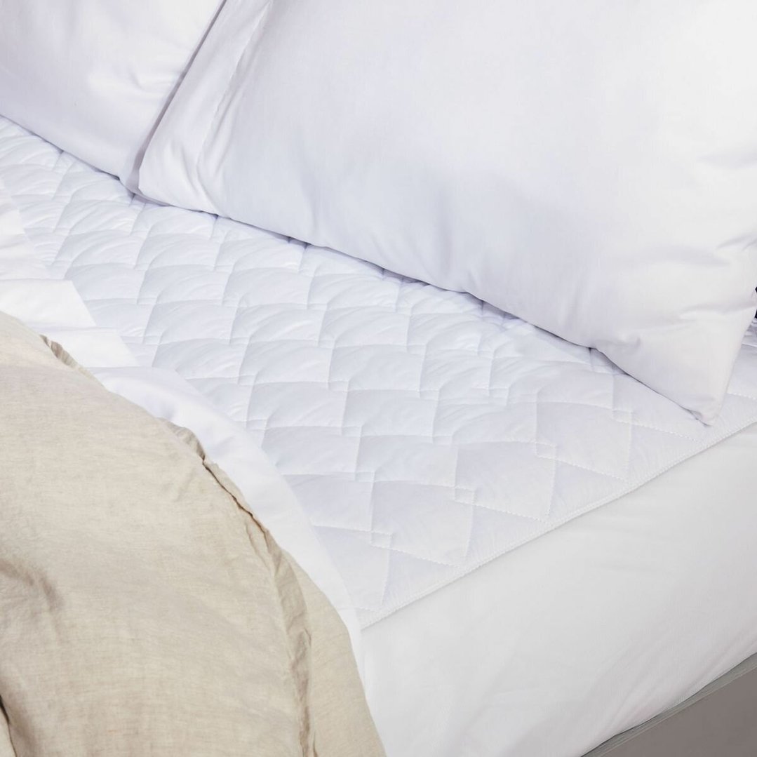 Close-up of a white quilted electric blanket on a bed with pillows and a duvet