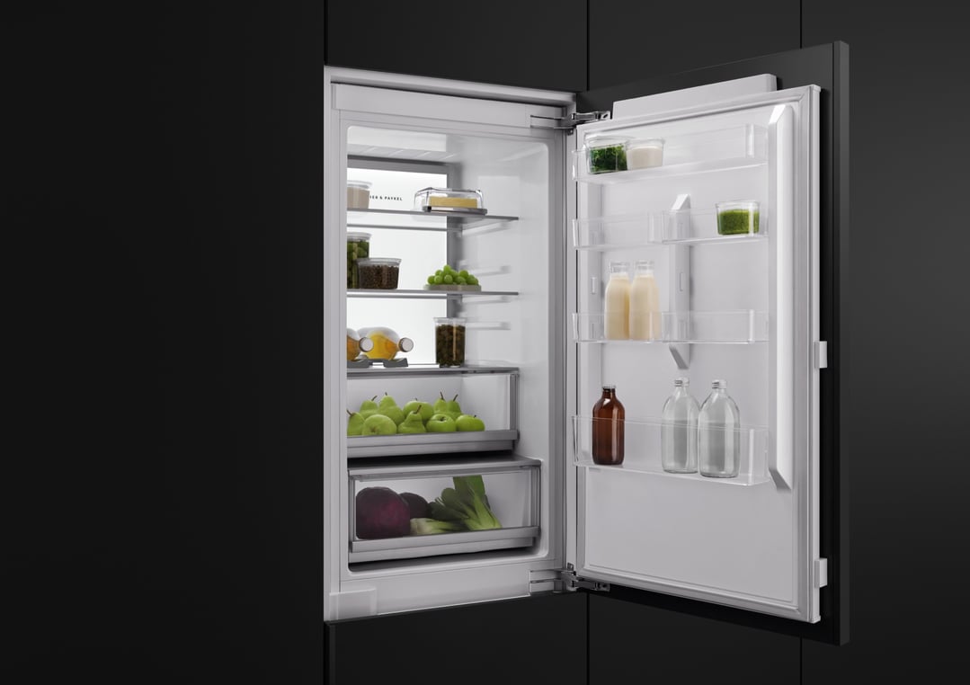 Open integrated refrigerator freezer filled with fresh food in a dark kitchen