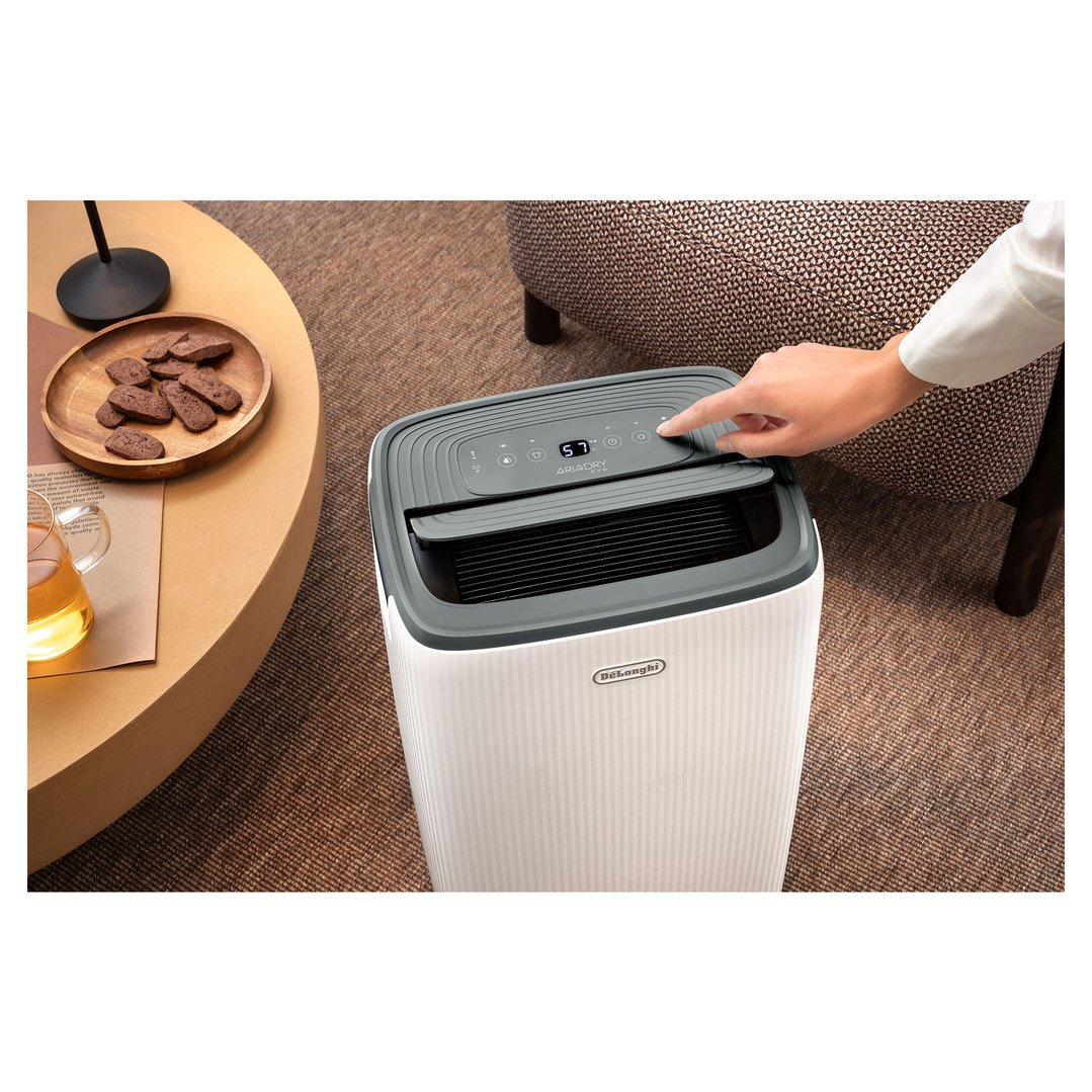 Hand adjusting controls on a DELONGHI Dehumidifier in a living room setting