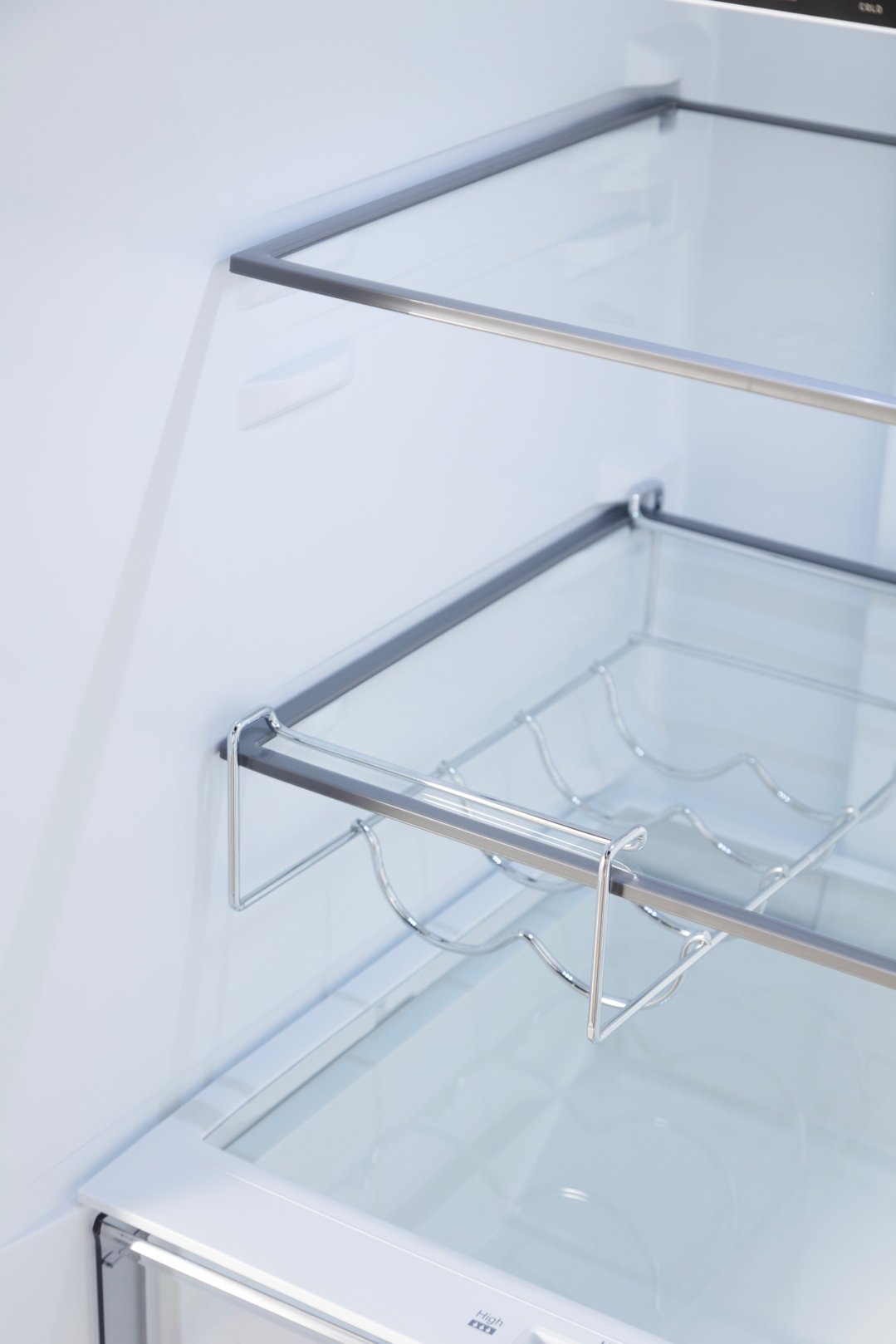 Interior view of a fridge showing glass shelves and a wine rack