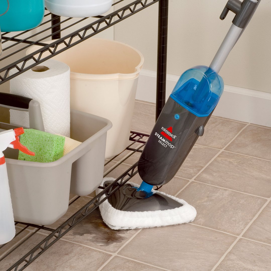 BISSELL Steam Mop Select cleaning a dirty tiled floor next to a storage shelf
