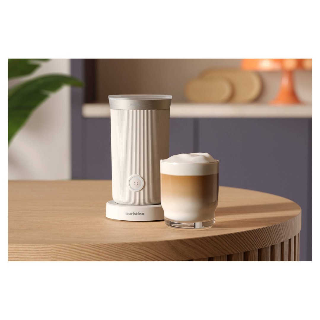 Baristina milk frother and a glass of latte on a wooden table