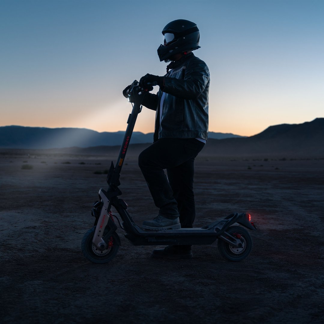 Person in helmet and jacket standing with an electric scooter at dusk