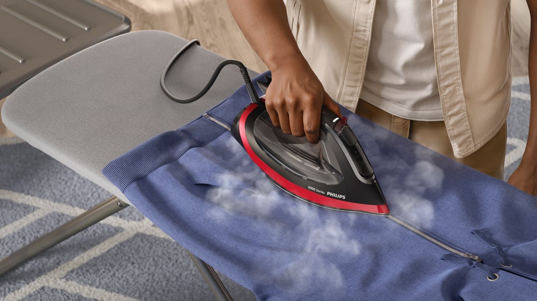 Person ironing a blue garment on an ironing board with a Philips steam iron