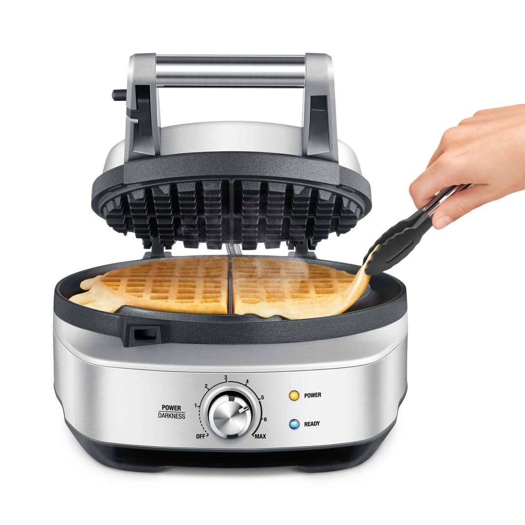 Hand using tongs to remove a waffle from an open waffle maker