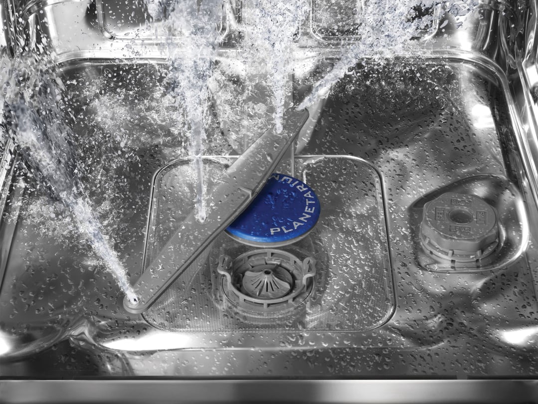 Inside a dishwasher, water sprays from the rotating arm during a wash cycle