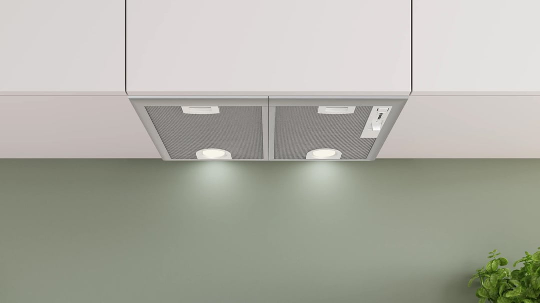 Integrated Bosch rangehood with lights on, installed under white kitchen cabinets