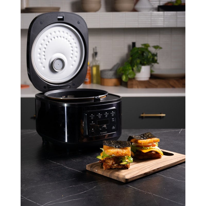 Black rice cooker with lid open on a kitchen counter with food