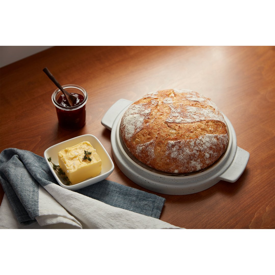Freshly baked bread in a bread bowl with butter and jam on a wooden table