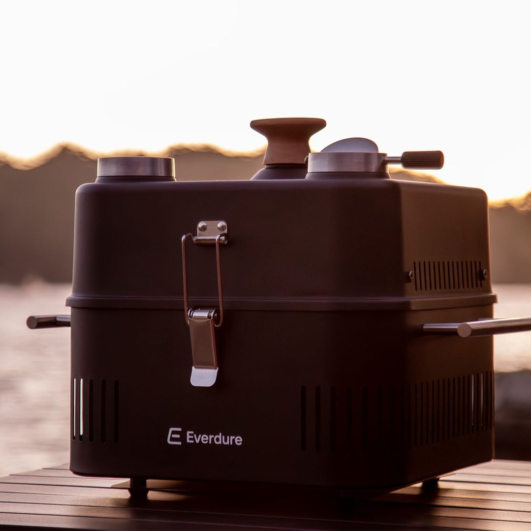 EVERDURE CUBE 360 portable charcoal BBQ on a wooden table outdoors at sunset
