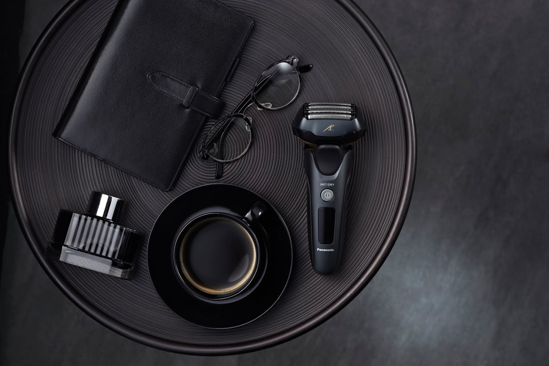 Panasonic shaver, coffee cup, notebook, and glasses on a dark textured table