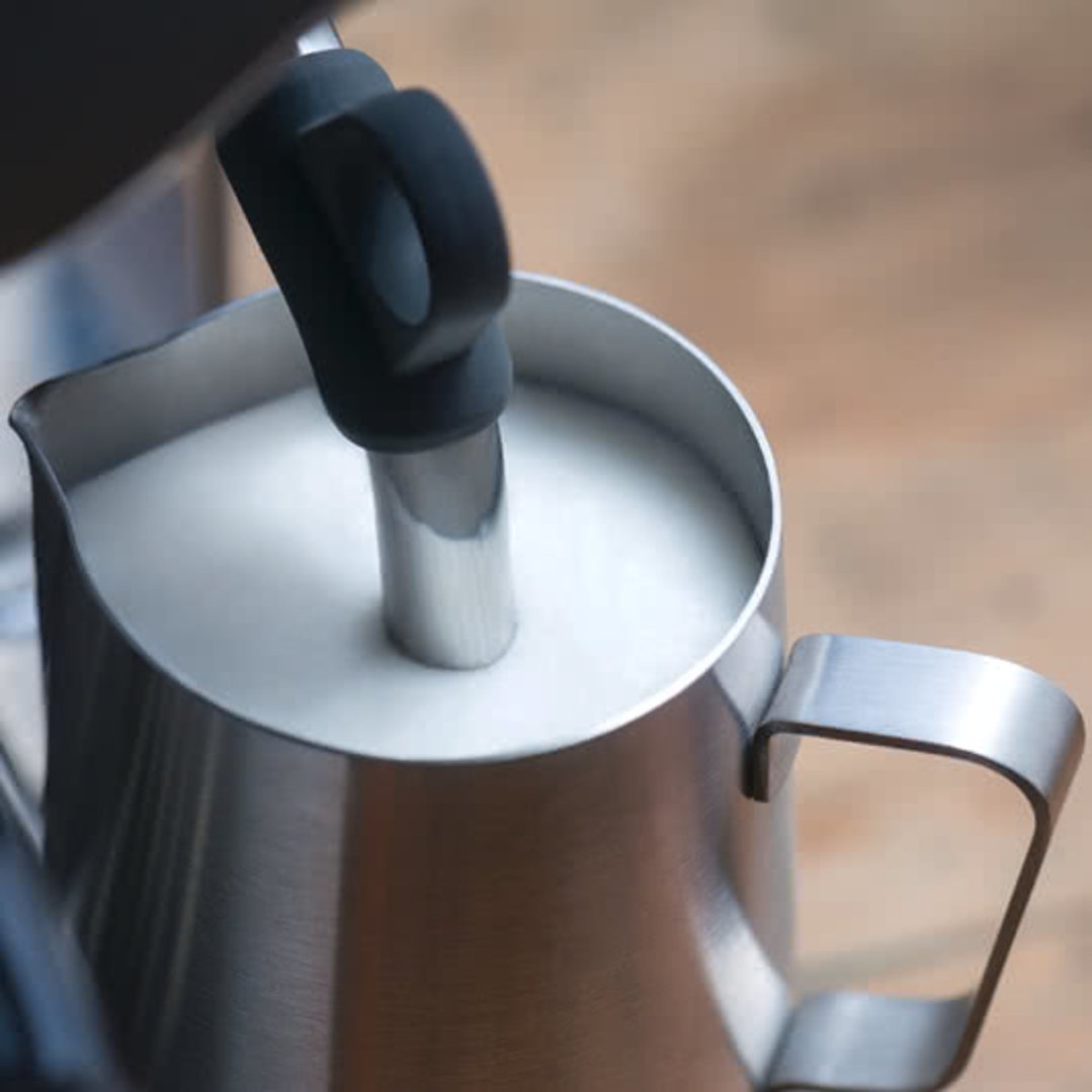 Close-up of a coffee machine's steam wand frothing milk in a metal jug