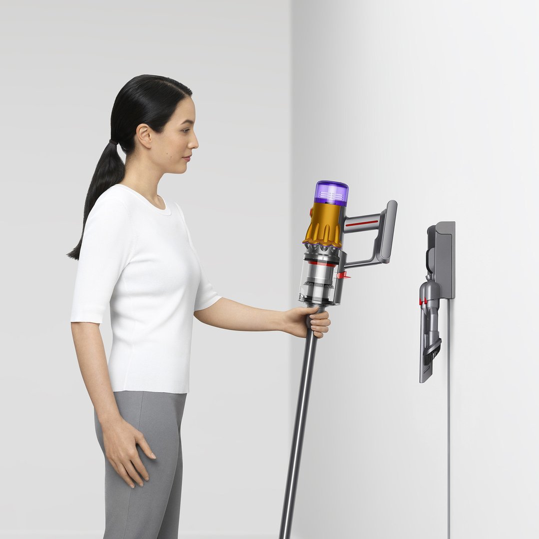 Woman holding a Dyson V12 Detect Slim stick vacuum next to its wall-mounted dock