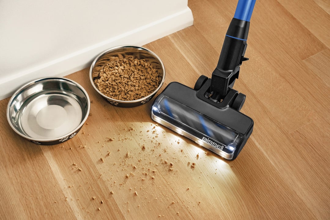 Handstick vacuum cleaning up spilled pet food next to two pet bowls