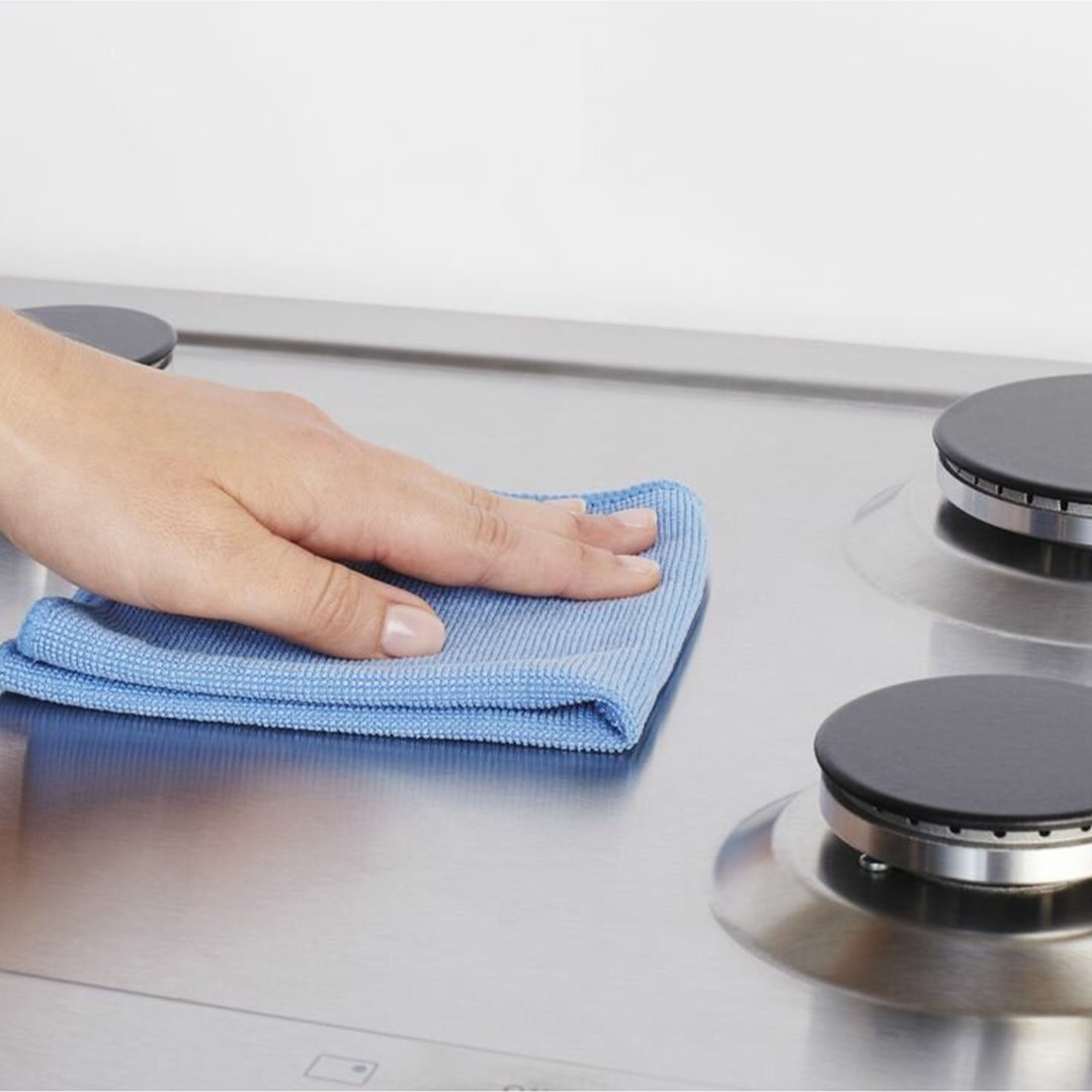 A hand wiping a stainless steel gas cooktop with a blue cloth