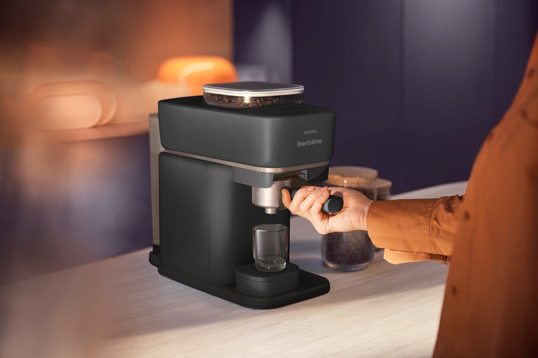 Hand operating a black Philips Baristina Espresso Machine on a kitchen counter