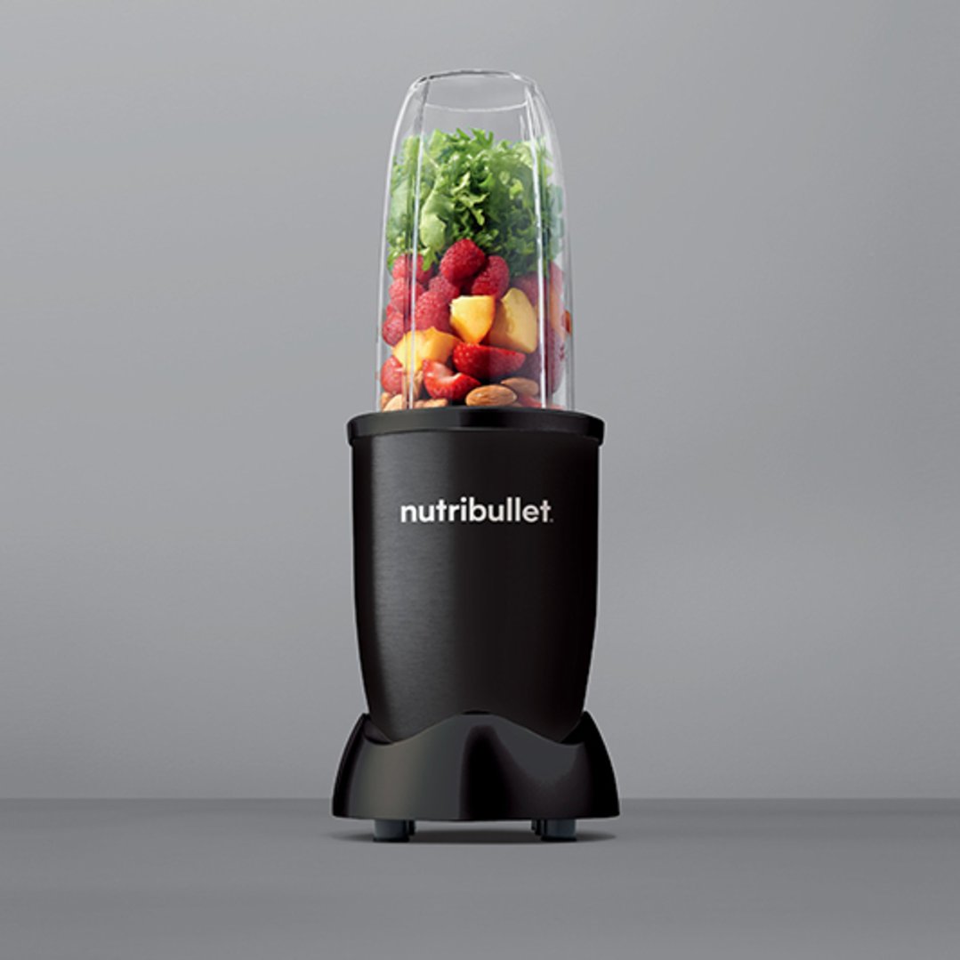 Black Nutribullet blender with fruit and greens in cup on a gray surface